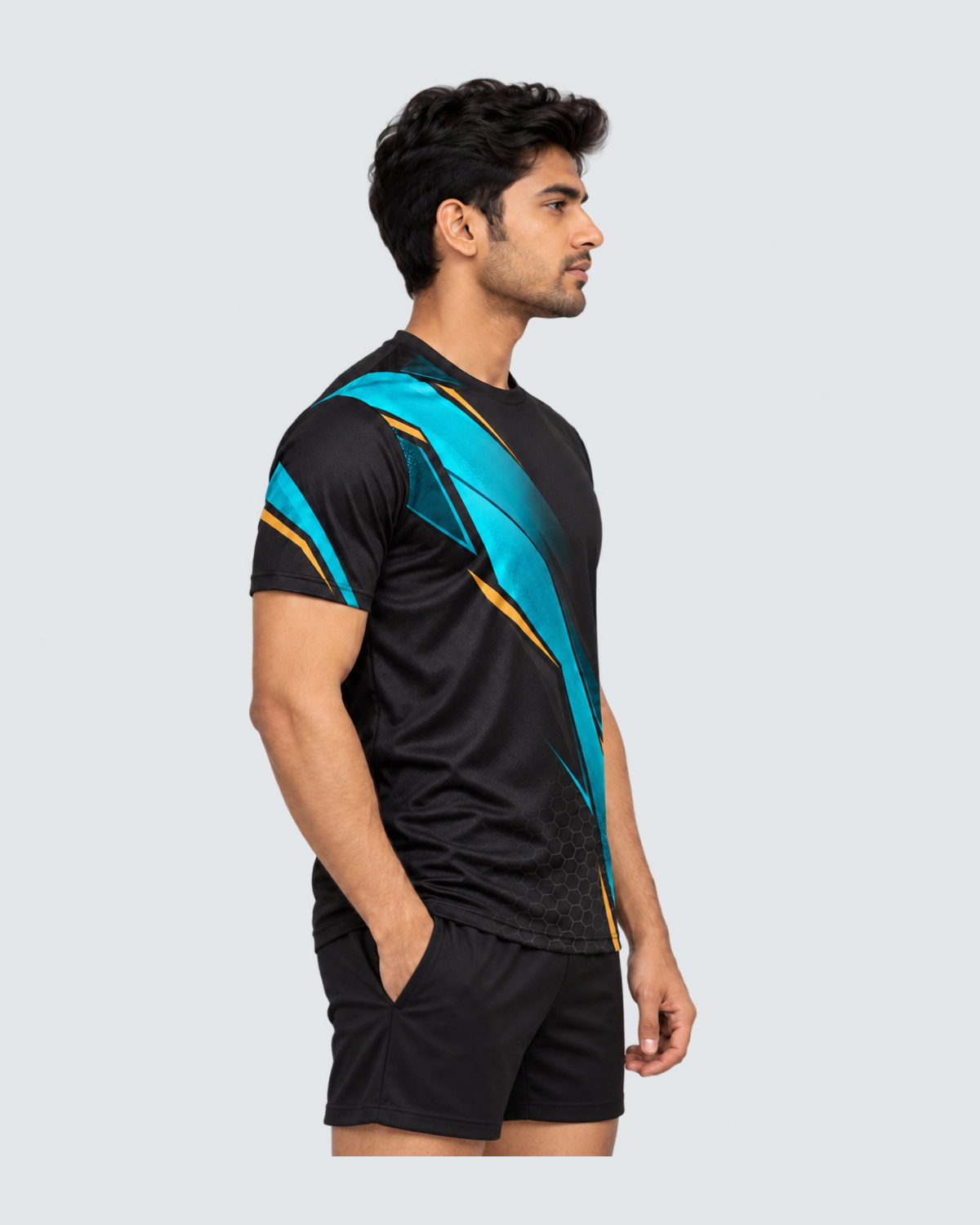 Carbon Tide, Left profile; Indian male model, black sports shorts, solid #E4E7E9 background, portrait 4:5