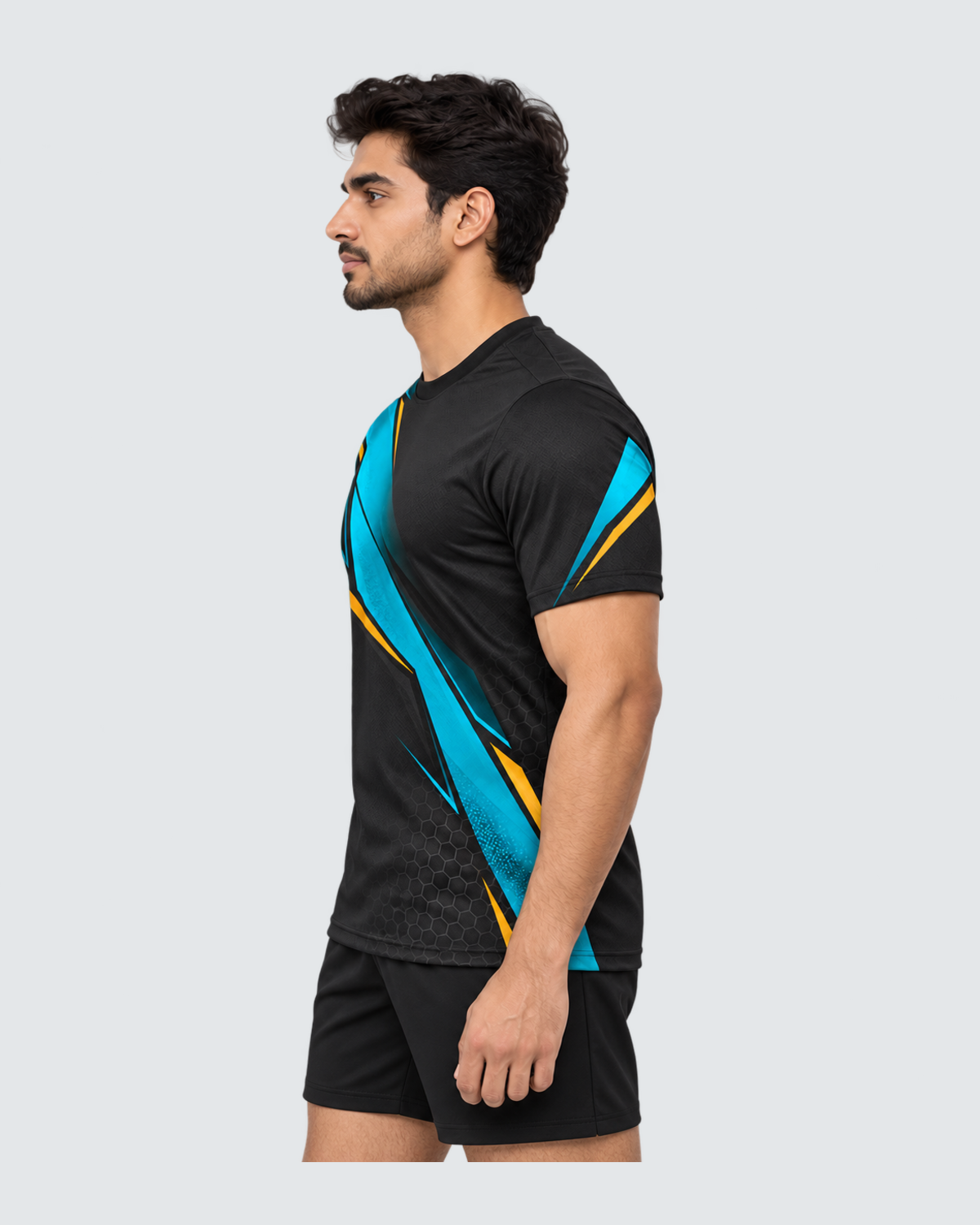 Carbon Tide, Opposite profile; Indian male model, black sports shorts, solid #E4E7E9 background, portrait 4:5